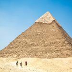 people riding a camel near pyramid under blue sky